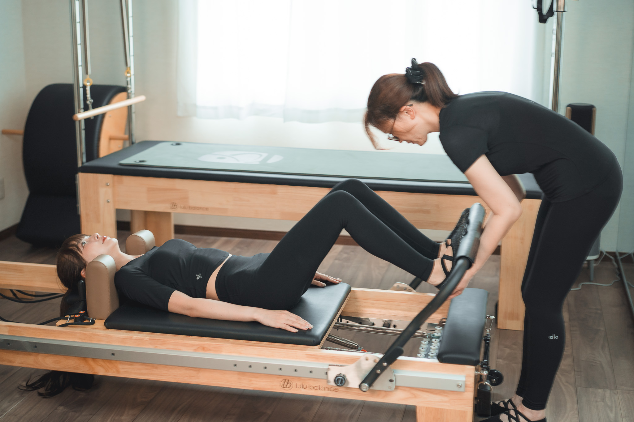 女性インストラクターがリフォーマーのレッスンをサポートしている様子